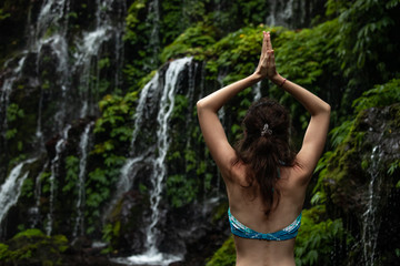 Close up of yoga woman raising arms with namaste mudra in front of waterfall. View from back. Banyu Wana Amertha waterfall Wanagiri, Bali, Indonesia.