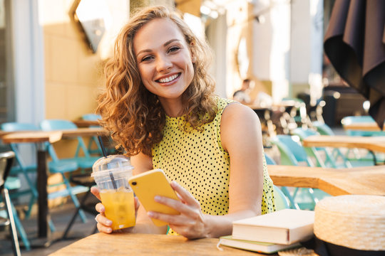 Image of woman holding cellphone in street summer cafe with cocktail