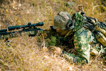 Man in uniform with sniper rifle, side view. Airsoft soldier lay in long grass and check wind correction in note