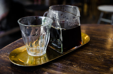 black coffee in glass pitcher on golden plate on wooden table