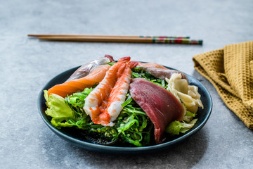 Sashimi Salad with Wakame, Seaweed, Salmon, Sea Bass, Shrimp, Kani, Mackerel Fish, Tuna served with Chopsticks.