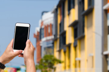 Hands are holding touch screen smart phone on blurred old building background.