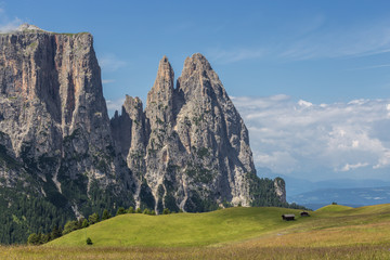 Landscapes on Alpe di Siusi with Schlern Mountain Group in Background and small cabins on the grassland in Summer, South Tyrol, Italy
