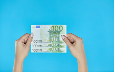 Female hands holding euro banknotes on blue background.