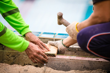 Close up workers are nailing on wooden board with hammer on construction site