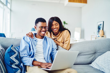 Cheerful african american young marriage laughing while watching movie on laptop computer at home...