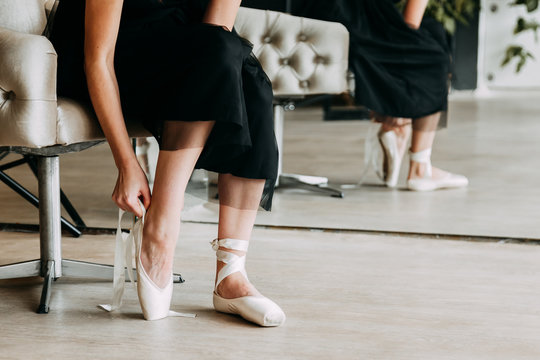 Close-up shot of a ballerina taking off the ballet shoes sitting on the floor in the studio.