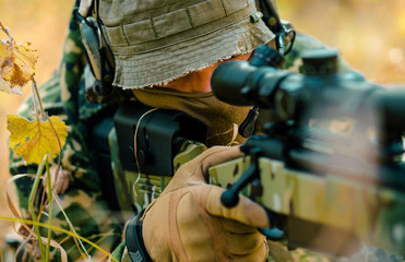 Closeup man in uniform with sniper rifle. Airsoft soldier lay and aims at the sight in long grass