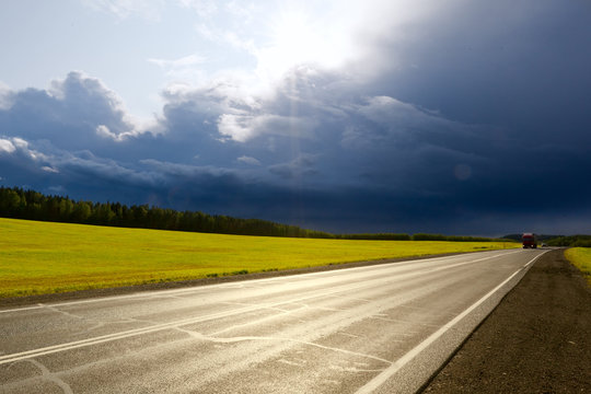 Thunderstorm front over a field and asphalt road in the sun