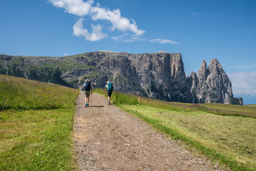 A couple hiking on the rural road in Alpe di Siusi, Seiser Alm, South Tyrol, Italy