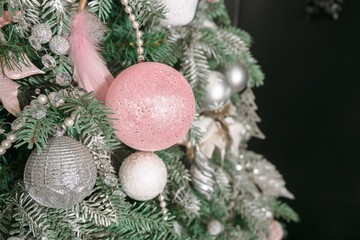 Fototapeta na wymiar Christmas tree decorated with toys in silver and pink color. In it we see the balloons with of ribbons, stick figure deer, beads and lights glowing garland, Christmas Tree is Ready for the Holiday