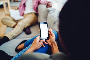Cropped image of dark skinned woman holding modern smartphone with mock up screen sitting on sofa at home, female using mobile phone connected to 4G internet checking notification from social networks