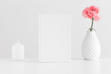 White book mockup with a pink carnation and a candle on a white table.