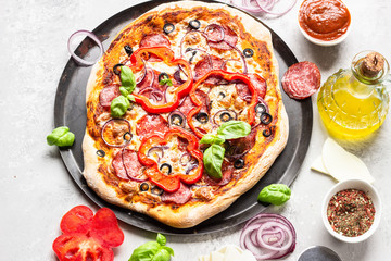 Tasty pizza with salami, onion, pepper, olives, mozzarella cheese and basil on black tray. Homemade hot pepperoni pizza.