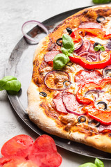 Tasty pizza with salami, onion, pepper, olives, mozzarella cheese and basil on black tray. Homemade hot pepperoni pizza.