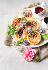 Cottage cheese pancakes or curd fritters with blackberries, melted chocolate and mint on ceramic plate. Traditional Ukrainian and Russian syrniki. Gourmet Breakfast.