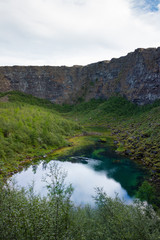 Fototapeta na wymiar High vertical walls of abyss and clear glacial lake in the valley, Iceland Asbyrgi canyon
