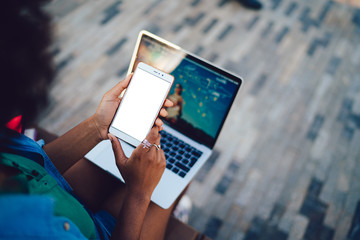 Close up view of woman holding smartphone with blank mock up screen for web design content front open laptop. Female hands with mobile phone, internet and applications, online shopping, chatting app