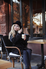 Fototapeta na wymiar Young beautiful woman in hat sitting in a cafe and drinking a cappuccino.