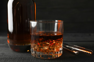 Bottle and glass of whiskey on wooden background, space for text