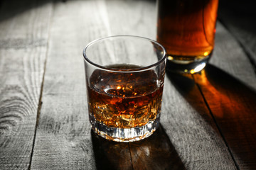 Bottle and glass of whiskey on wooden background, space for text