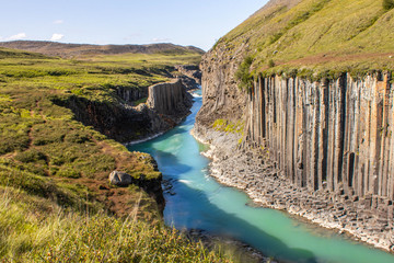 Recessed clear cyan river in grass mountains, canyun with basalt columns in Iceland, Studlagil...