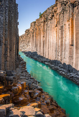 Clear turquoise and cyan river flowing through high basalt colmun canyon in Iceland, Studlagil...