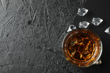 Glass of whiskey and ice cubes on black background, top view