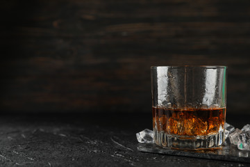 Glass of whiskey and ice cubes on black background, space for text