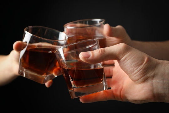 Three Male Hands Holds Glasses Of Whiskey On Black Background, Close Up. Cheers