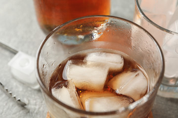 Bottle, glasses with ice cubes and whiskey on grey background, close up