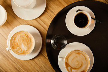 top view of cups of different coffee near glass of water on tray