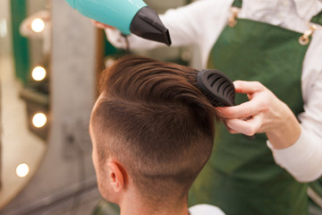 Hairdresser dries hair of stylish man.  Young handsome guy doing hair styling at a hairdresser