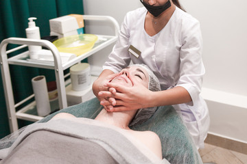 Doctor beautician makes cosmetic facial massage. Woman relaxes on a cosmetic chair side view