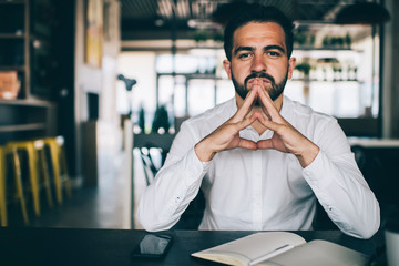 Portrait of serious Caucasian male entrepreneur in white shirt looking at camera while thinking on...