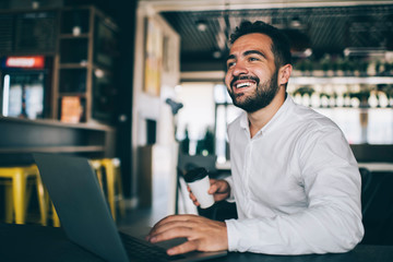 Happy male entrepreneur working remotely in public coffee shop with high speed inernet connection,...