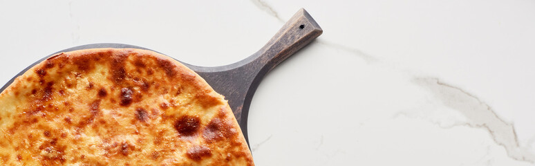 Top view of imereti khachapuri on chopping board on marble texture, panoramic shot