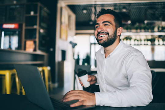 Happy male entrepreneur working remotely in public coffee shop with high speed inernet connection, skilled successful man laughing indoors using laptop computer for programming application