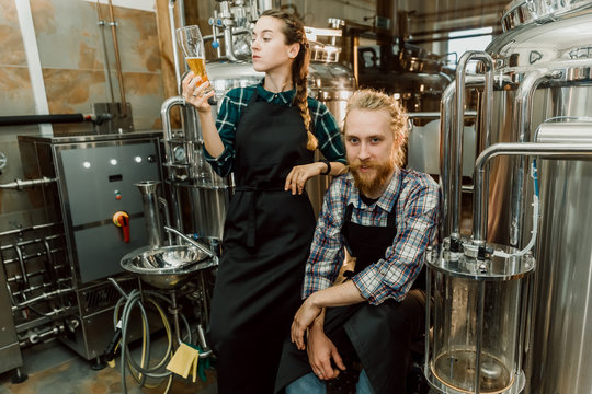 Brewery workers looking at freshly made beer in glass tube and discussing it. Male and female brewer testing beer at brewery factory. 4k. Small business concept. - Powered by Adobe