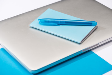 high angle view of colorful notebook, blue pen, laptop, paper on white background