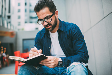 Serious man in optical eyeglasses making notes of ideas for online publication in textbook for...