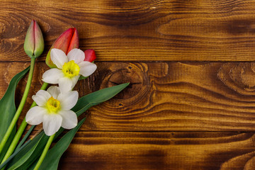 Fototapeta na wymiar Bouquet of daffodils and red tulips on wooden background. Greeting card for Easter, Valentine's Day, Women's Day and Mother's Day. Top view, copy space