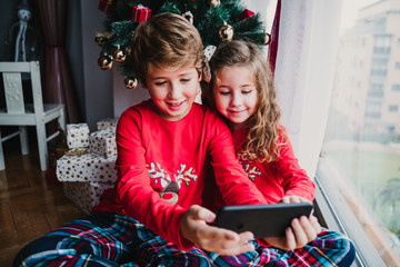 beautiful brother and sister at home taking a selfie with mobile phone. Happy kids sitting by the christmas tree