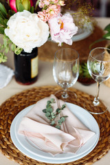 Fototapeta na wymiar Festive table. A plate on a straw stand, a pink fabric napkin and a eucalyptus branch on it