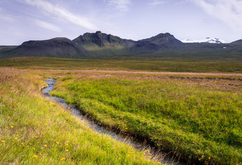 Stream flowing on meadow field, high mountains in background