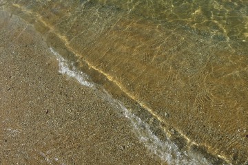 The waves beat at the beach with sand and reflection of sunlight in summer morning. Nature background concept.