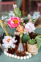 Festive table setting. Brightly colored peonies in a vase with brown glass, wooden beads nearby