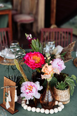 Fototapeta na wymiar Festive table setting. Brightly colored peonies in a vase with brown glass, wooden beads nearby