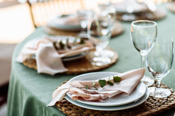 Festive table setting. Plates decorated with eucalyptus branches and elegant napkins in nude colors.