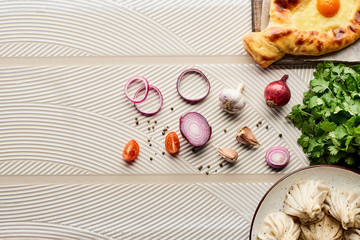top view of delicious khinkali and adjarian khachapuri near vegetables and spices on beige textured background